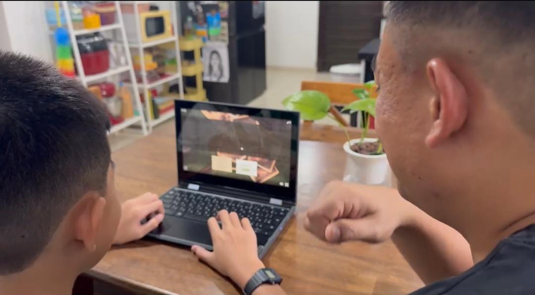Seorang bapa menemani anak lelaki belajar di hadapan komputer riba